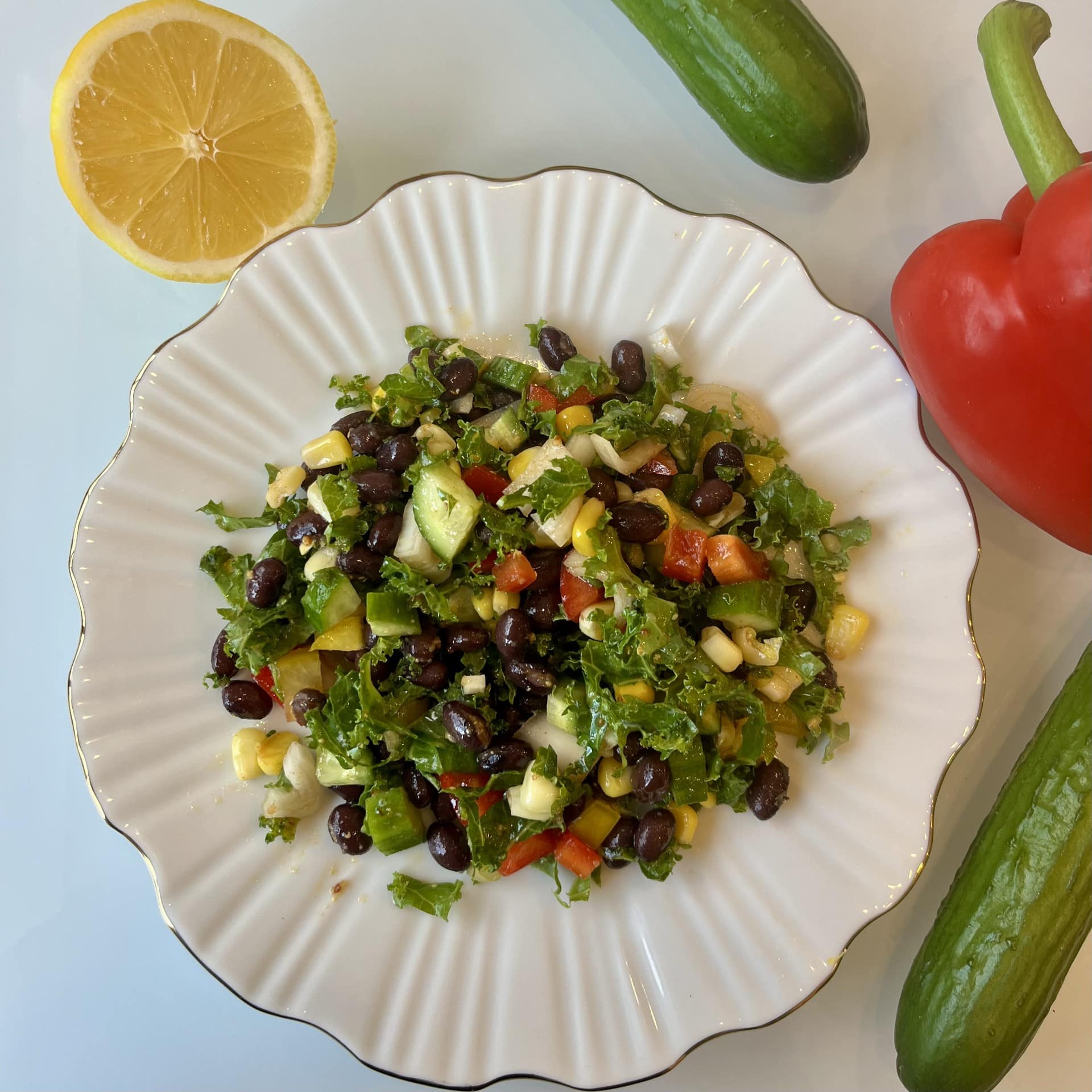 A vibrant longevity bowl featuring finely chopped kale, black beans, colorful bell peppers, corn, cucumbers, and red onion, all tossed in a smoky lemon paprika dressing and served in a white bowl. The salad is fresh, colorful, and nutrient-dense